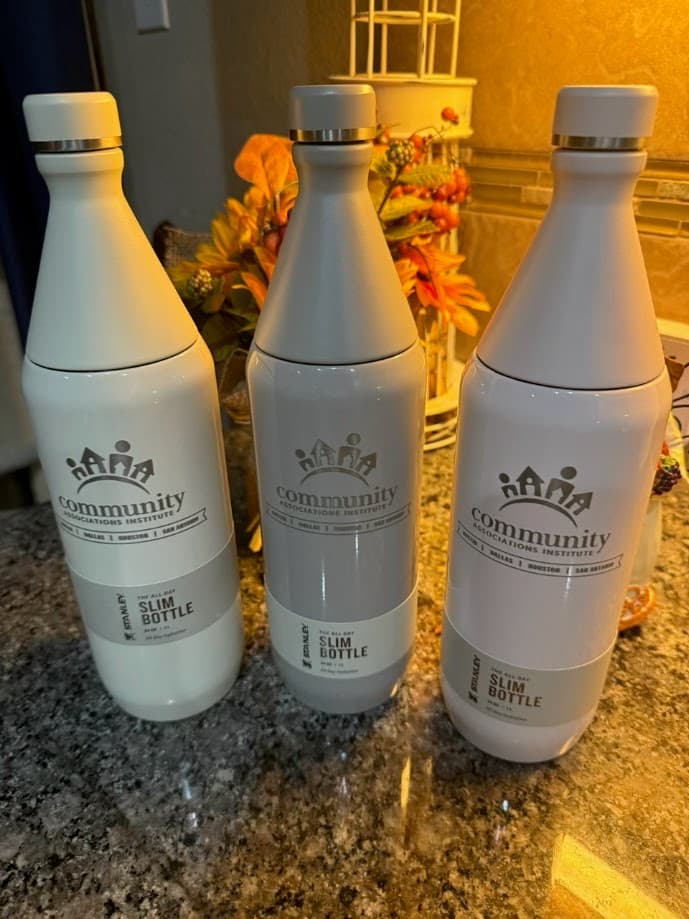Three Stanley slim bottles with Community Associations Institute logos standing on a granite countertop.